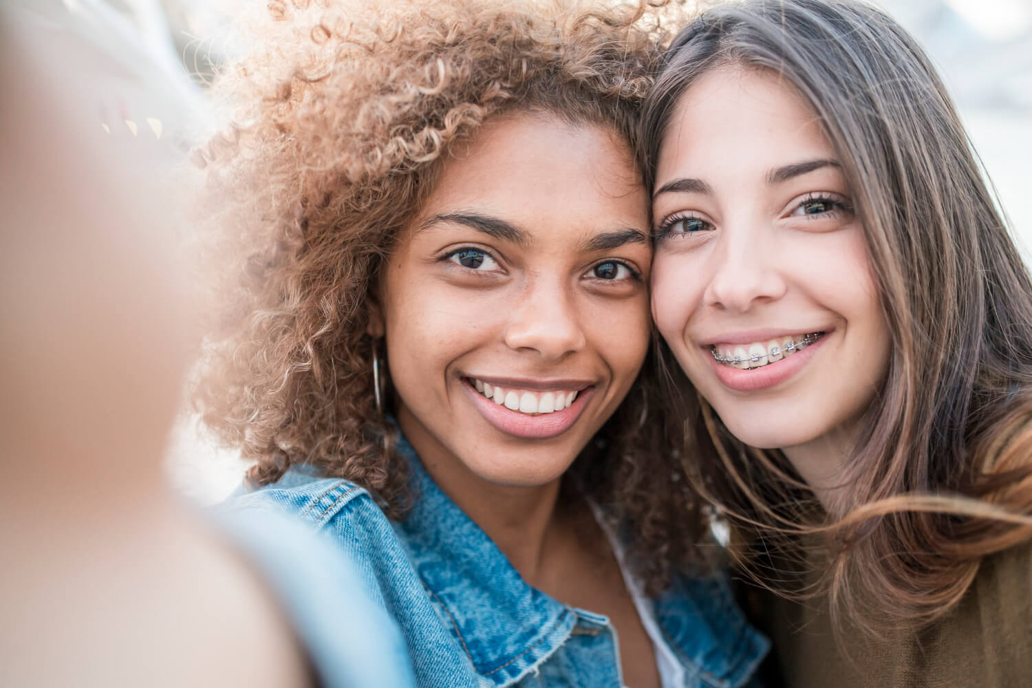 Duas amigas sorrindo em selfie de close, uma com cabelo cacheado e a outra com aparelho fixo, comparando com alinhadores invisíveis em Botafogo.